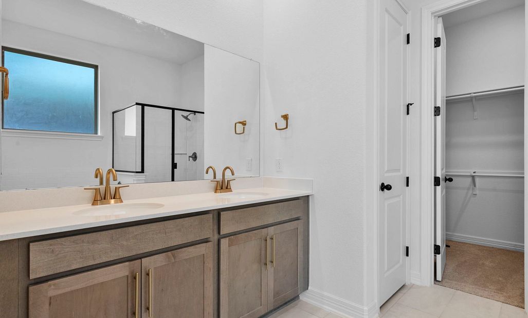 Serene and stylish primary bath with double vanity, warm stained cabinets with brass fixture, and