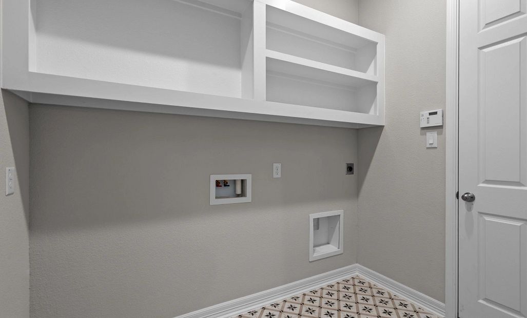 Organized and practical utility room featuring built-in shelves and laundry connections