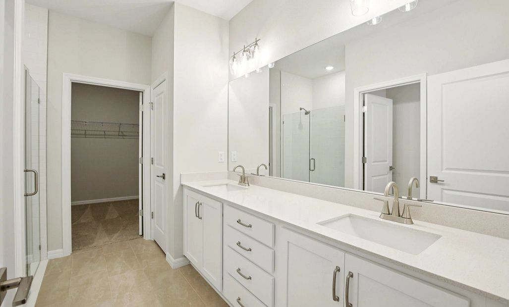Primary bathroom with double sinks, frameless shower, linen closet and large walk in closet