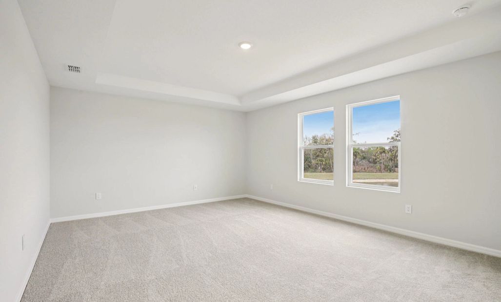 Large primary bedroom with double windows and a tray ceiling