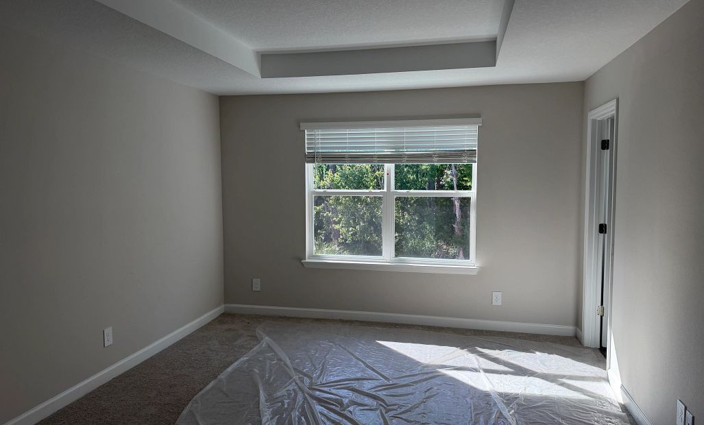 Primary bedroom with a tray ceiling and large double window - under construction