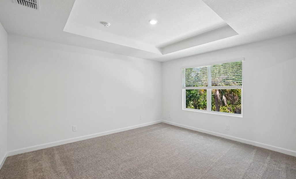 Primary bedroom with a tray ceiling and a beautiful view of the trees behind the townhome -