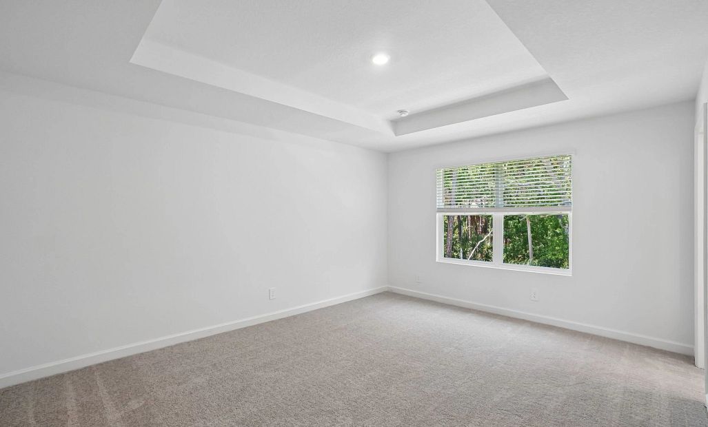 Primary bedroom with a tray ceiling looking out into the tree filled back view