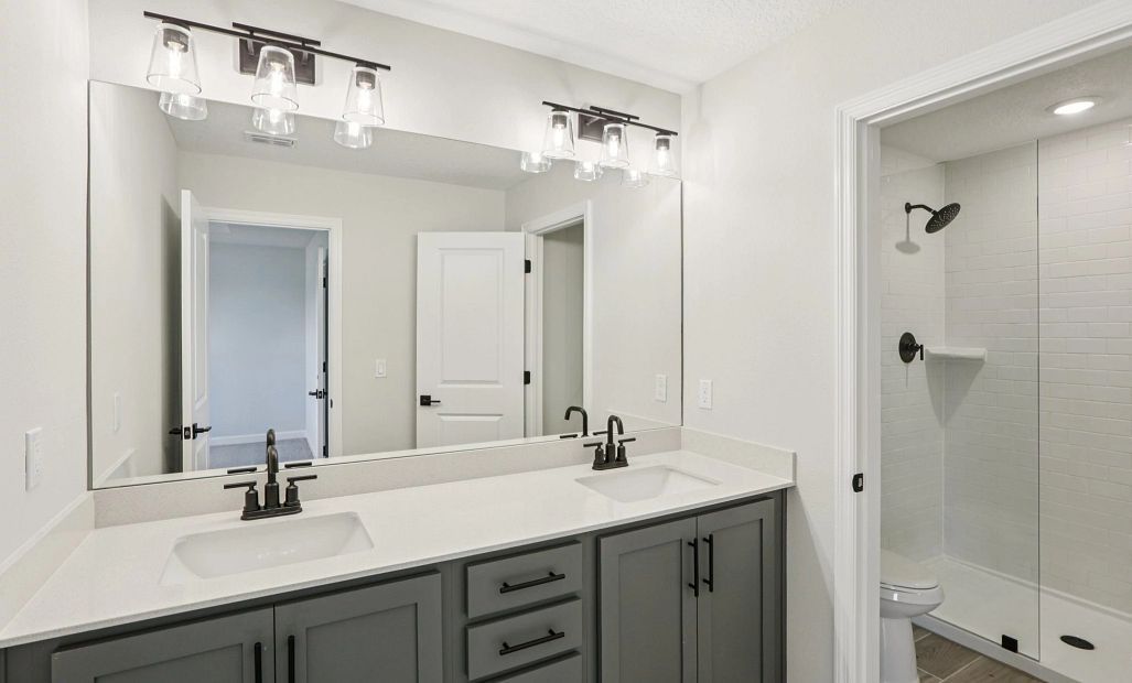 Primary bathroom with double sinks and a frameless walk-in shower featuring aspects of AW
