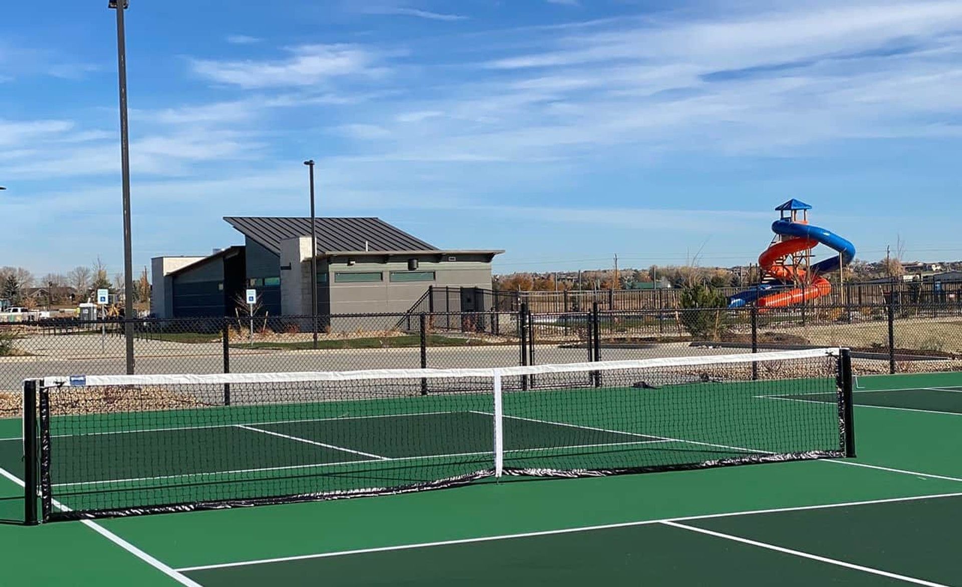 Luxury tennis court with sleek clubhouse and vibrant slide at Trailside on Harmony, Colorado.