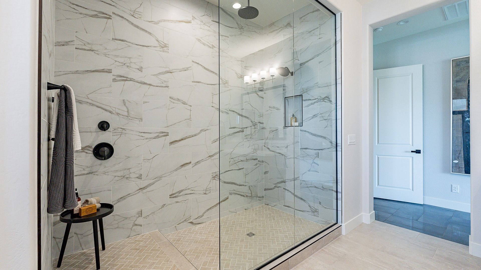 Opulent marble-tiled shower with sleek black fixtures and seamless glass in Windrose community.
