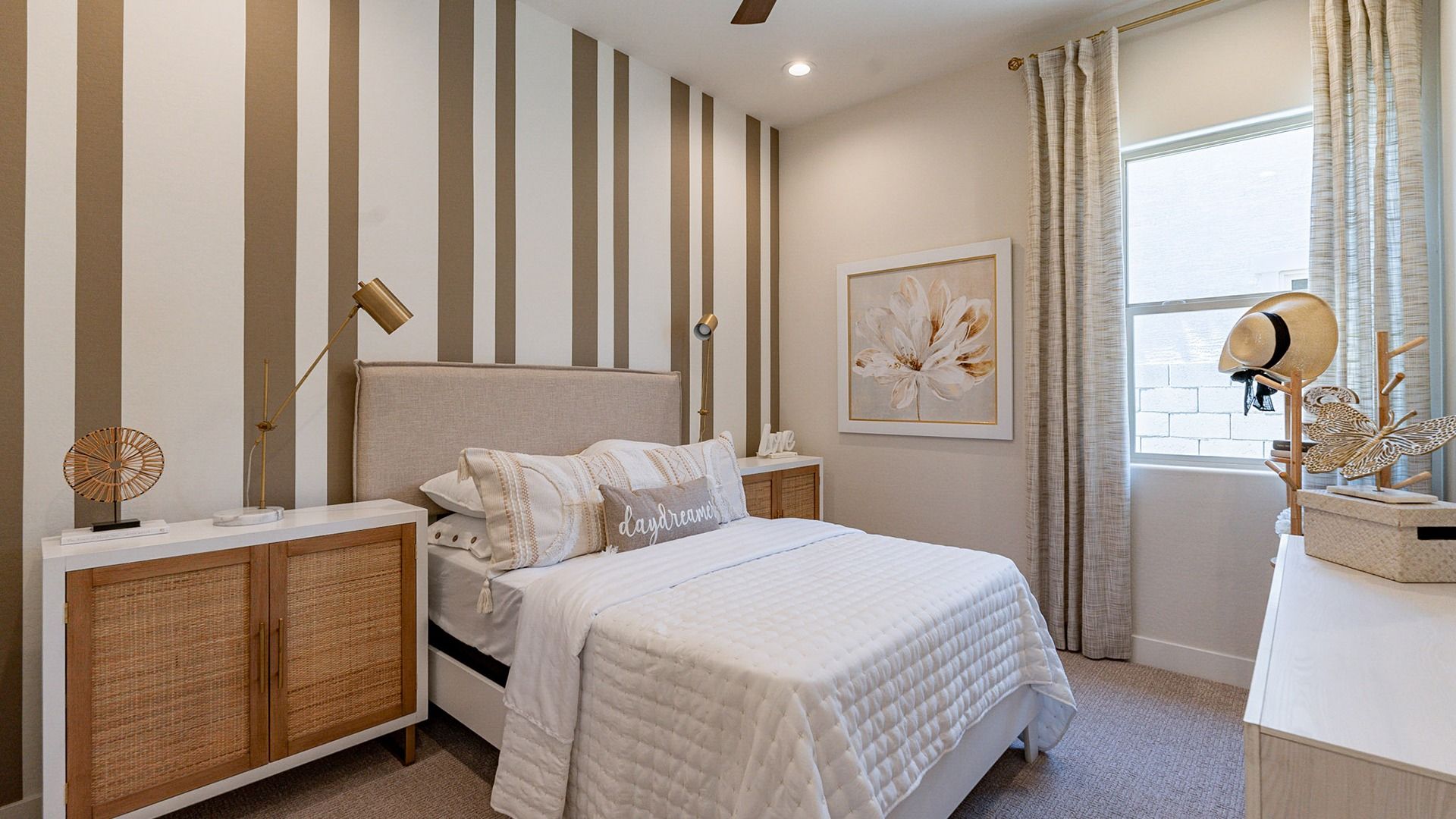Windrose bedroom boasts chic striped walls, plush beige headboard, and refined decor. Abundant natural light enhances luxury.