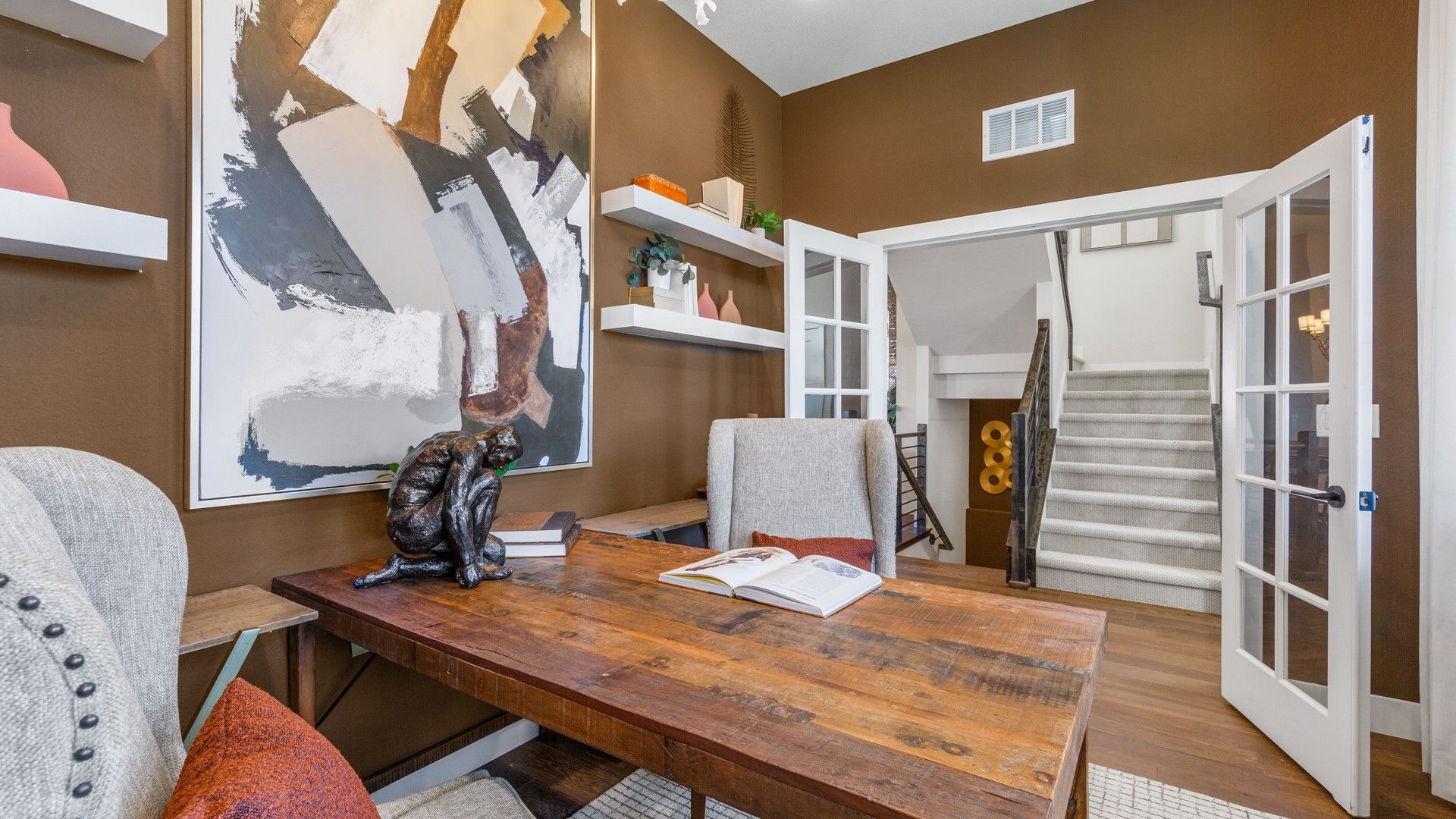 Elegant home office with a rustic wooden desk, abstract art, and chic staircase in Dillon Pointe.