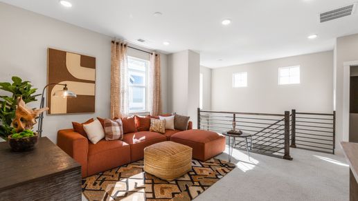 Sunlit living room boasts plush orange seating, sleek metal railings, and oversized windows. Dillon Pointe.