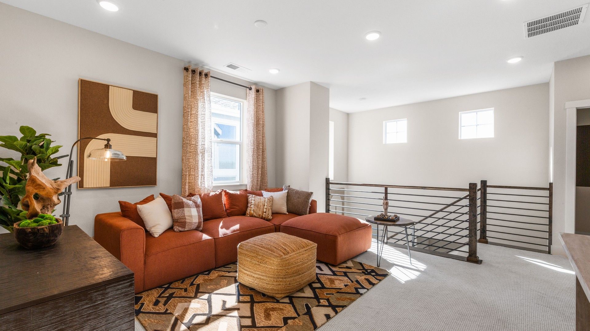 Sunlit living room boasts plush orange seating, sleek metal railings, and oversized windows. Dillon Pointe.