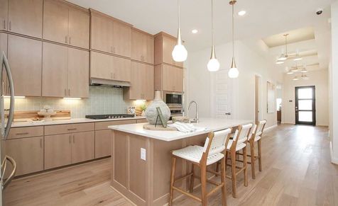 Experience luxury in Sunterra's kitchen featuring light wood cabinetry, sleek pendant lighting, and spacious island.
