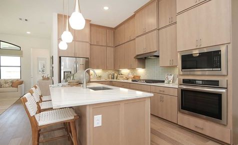 Elegant Sunterra kitchen boasts light wood cabinetry, sleek appliances, and a chic island centerpiece.