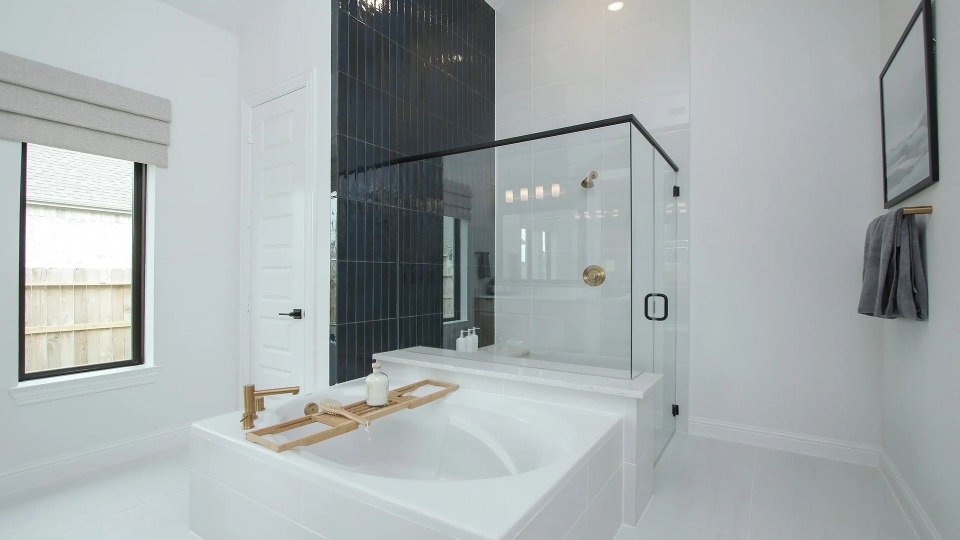 Experience elegance with a freestanding tub and gold fixtures against a striking black tile wall in Coastal Point.