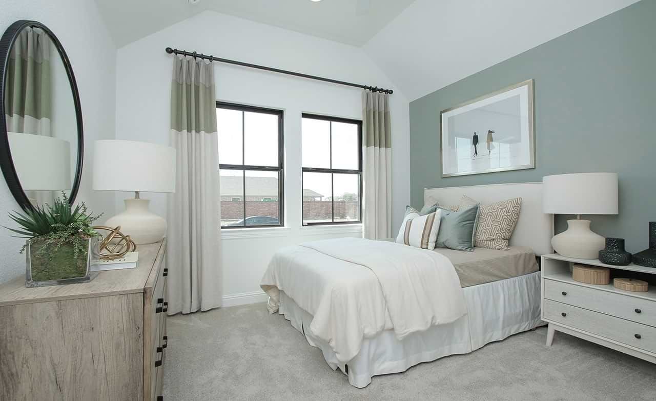 Sunterra bedroom boasts vaulted ceilings, elegant pale green accent wall, and expansive windows for airy luxury.