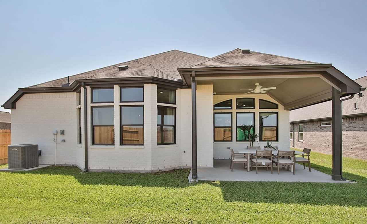 Spacious Sunterra residence features expansive windows and a refined, covered patio amid lush greenery.
