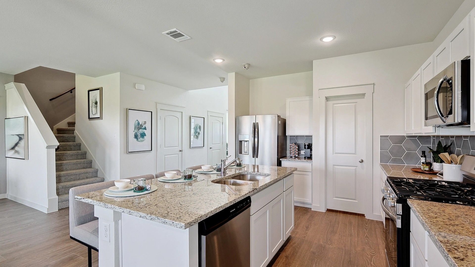 Luxurious kitchen in Patriot Estates features granite countertops, sleek island, hexagonal backsplash, and stainless steel appliances.