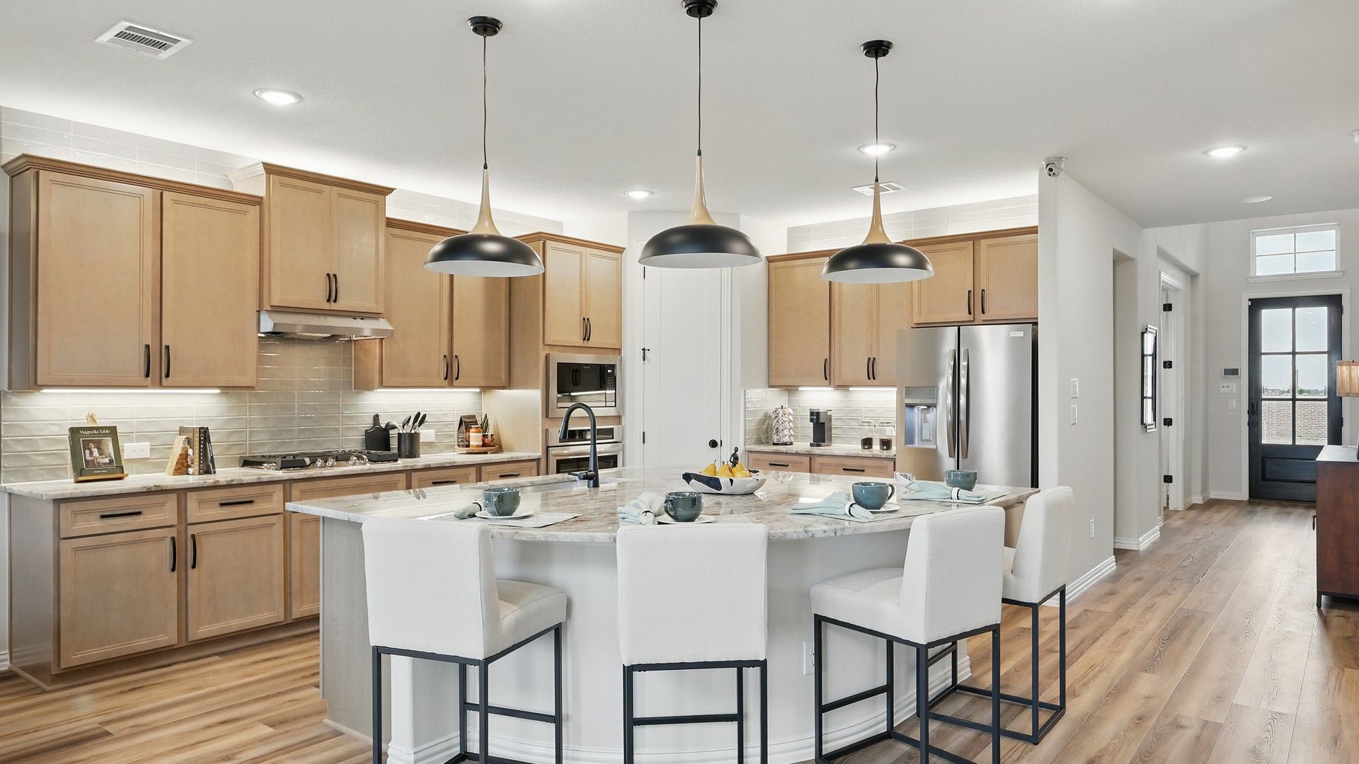 Elegant kitchen features marble island, sleek pendant lighting, lightwood cabinetry in Westridge community.