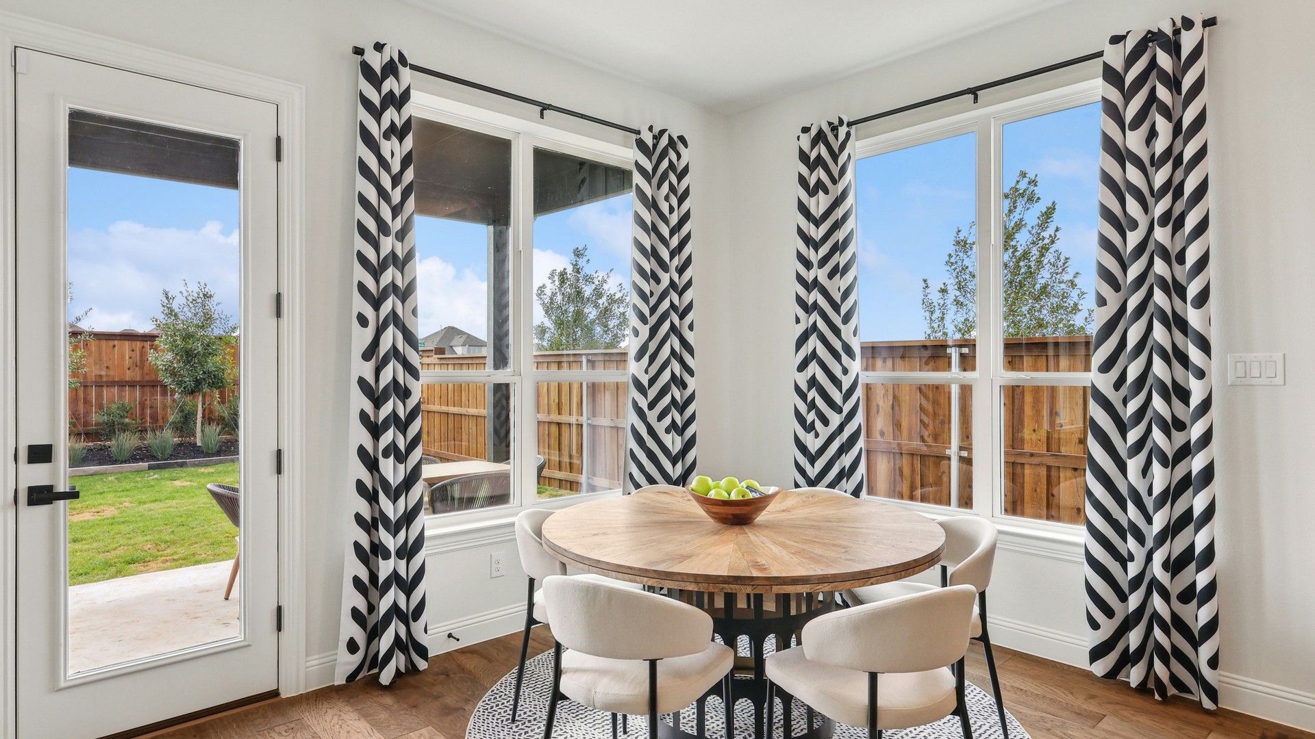 Revel in a chic dining area featuring a round wood table, striking curtains, and expansive windows in Green Meadows.