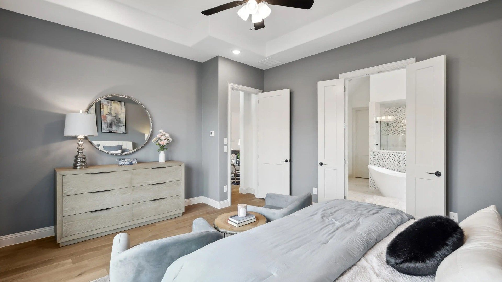 Stylish bedroom with tray ceiling, light wood floors, and elegant en-suite bathroom in Westside Preserve community.