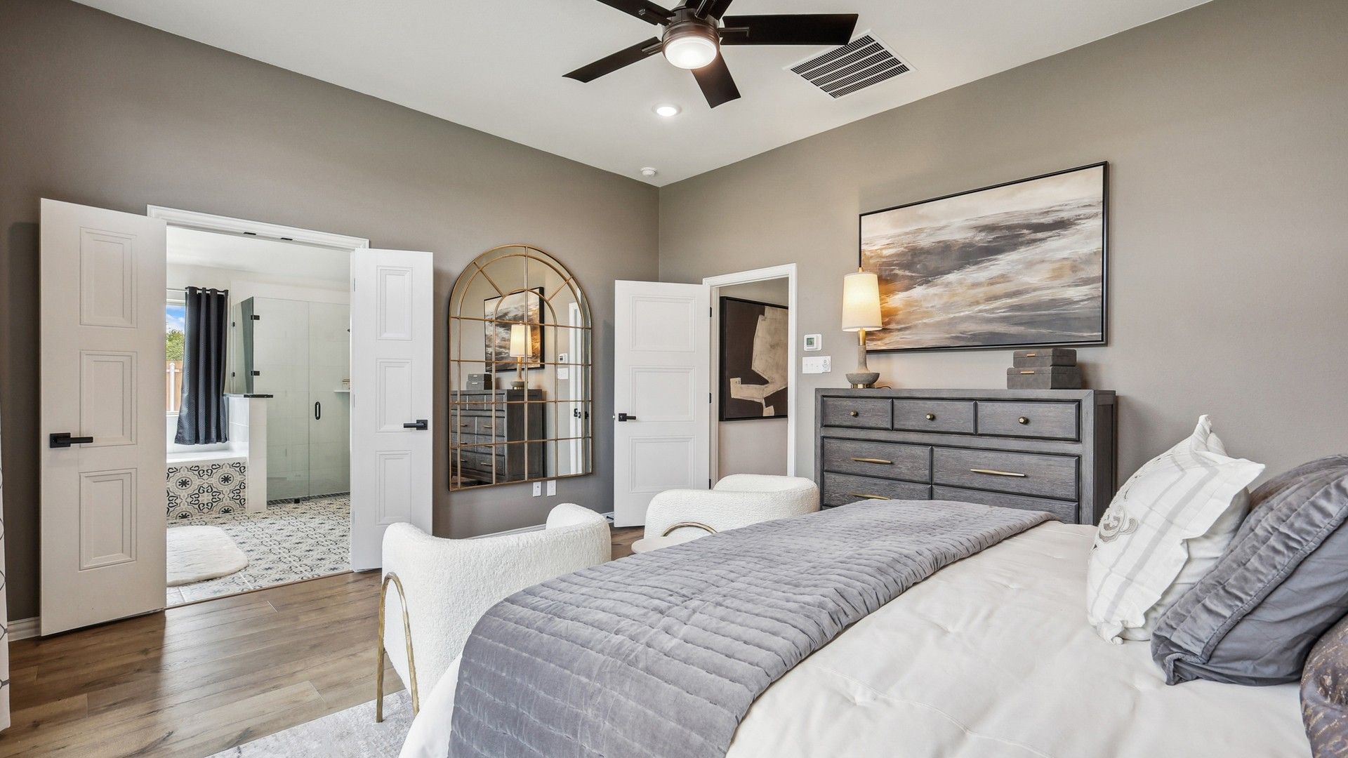 Elegant Churchill bedroom with ensuite bath, featuring a striking mirror, nuanced wood floors, and bespoke artwork.