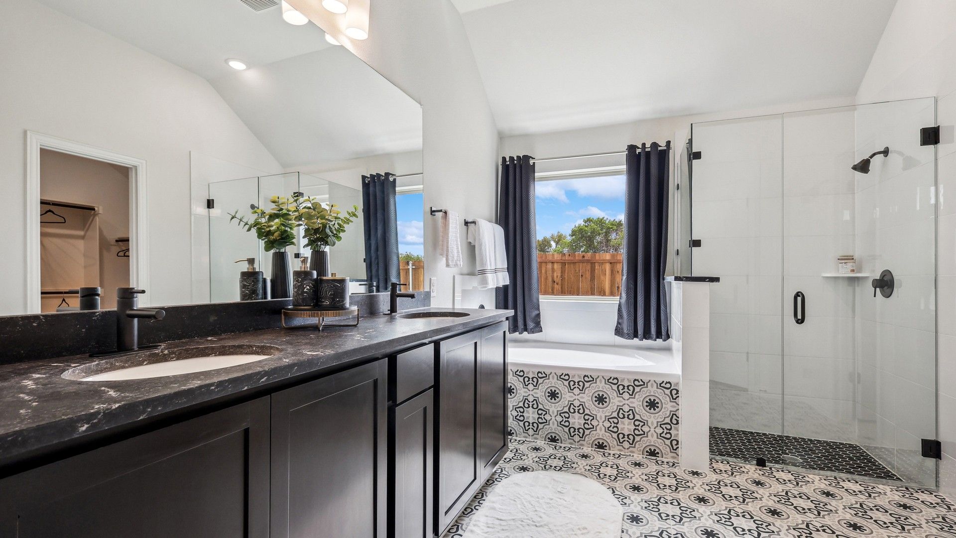 Indulge in elegance with a black marble vanity, intricate patterned tiles, and glass shower in Churchill Community.