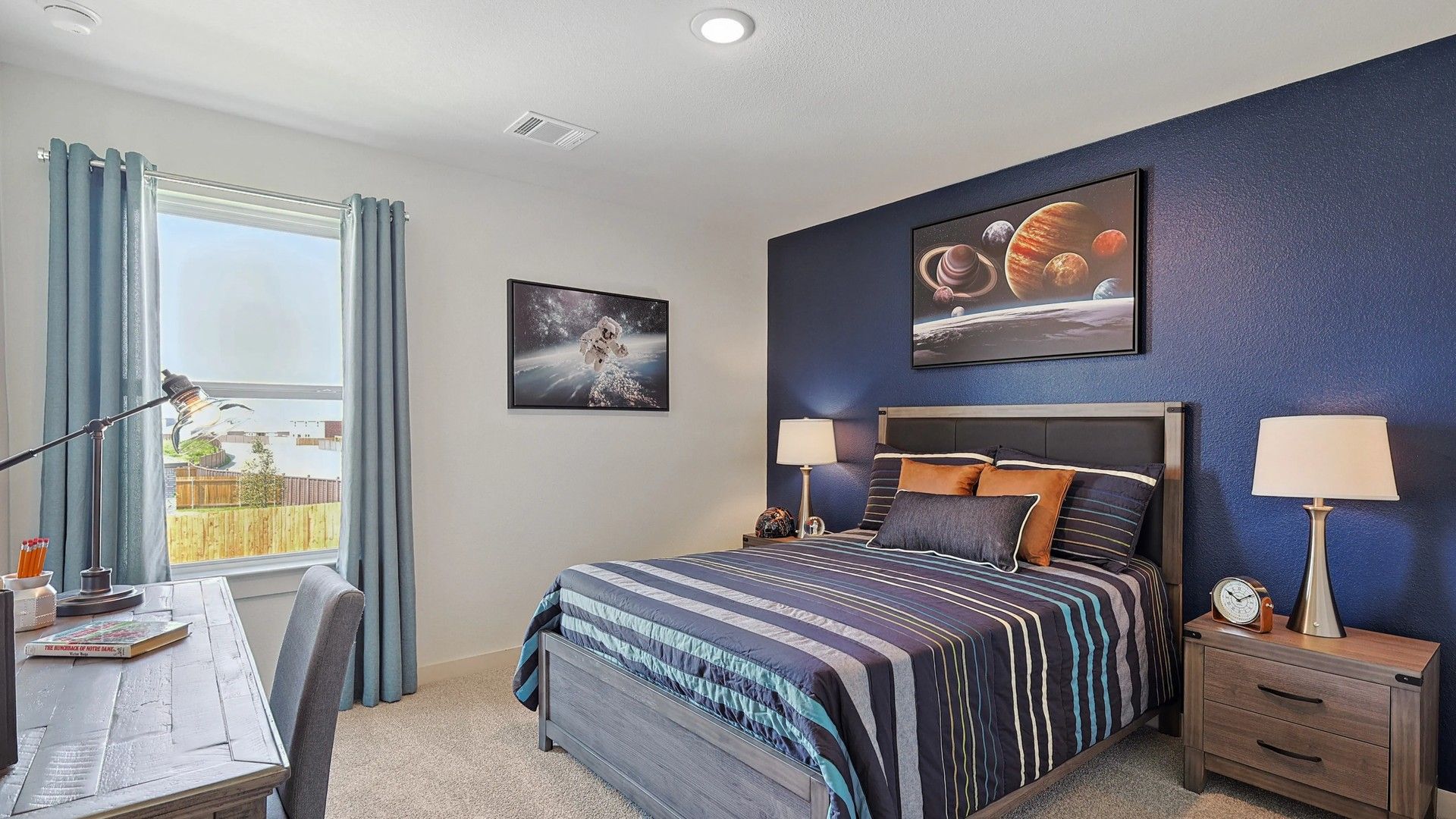Elegant bedroom features rich blue accent wall, luxury wood furniture, and space art in Patriot Estates.