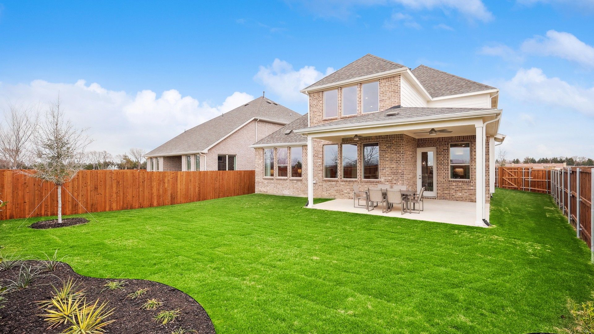 Elegant brick facade with expansive patio and lush lawn in The Oaks community. Luxurious outdoor living.