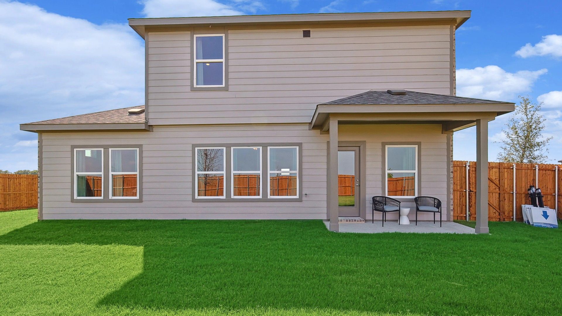 Elegant Patriot Estates residence featuring sleek beige siding and expansive windows, set in a spacious green yard.