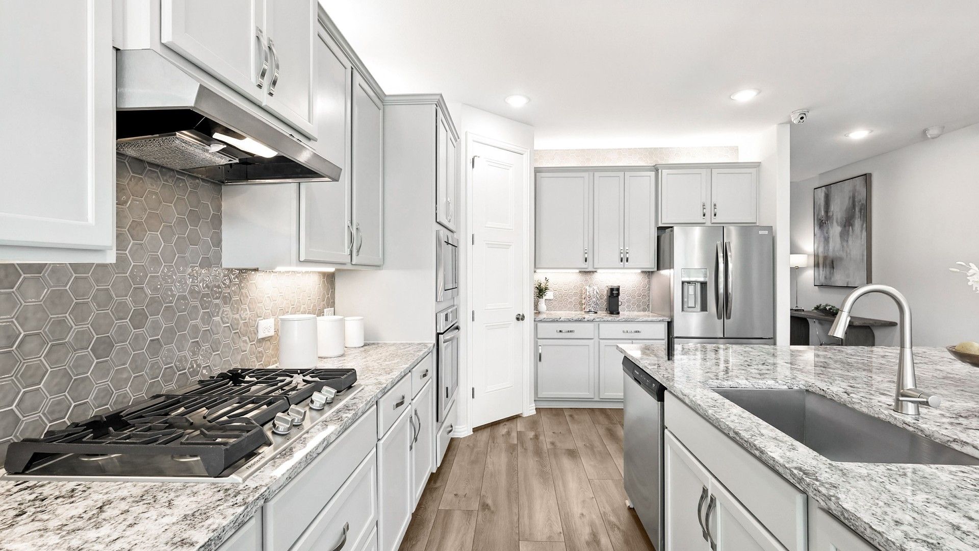Exquisite white cabinetry, hexagonal backsplash, and luxurious granite countertops define this Green Oaks Preserve kitchen.