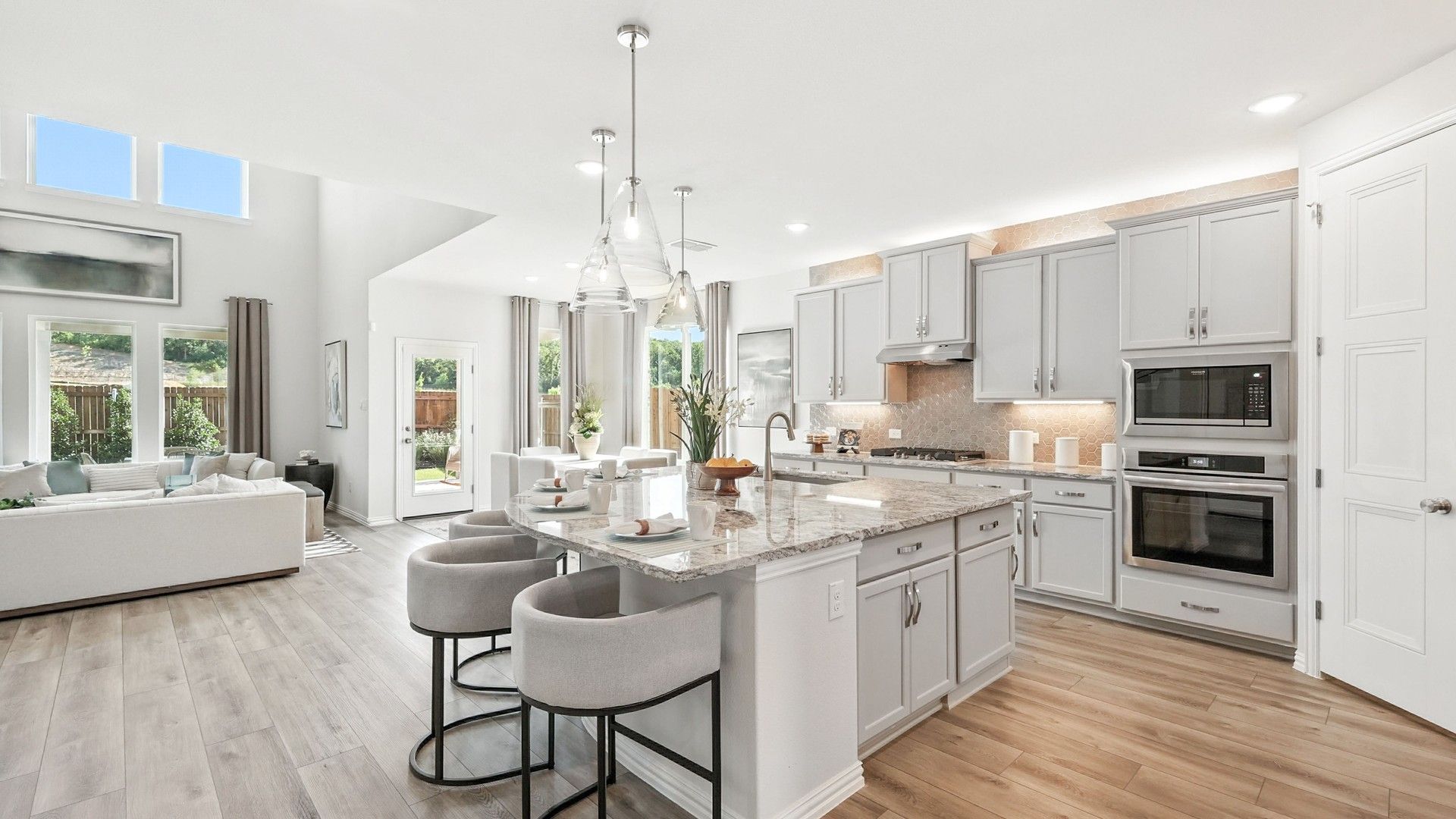 Opulent granite island, pristine gray cabinetry, and chic pendant lights in Green Oaks Preserve kitchen.