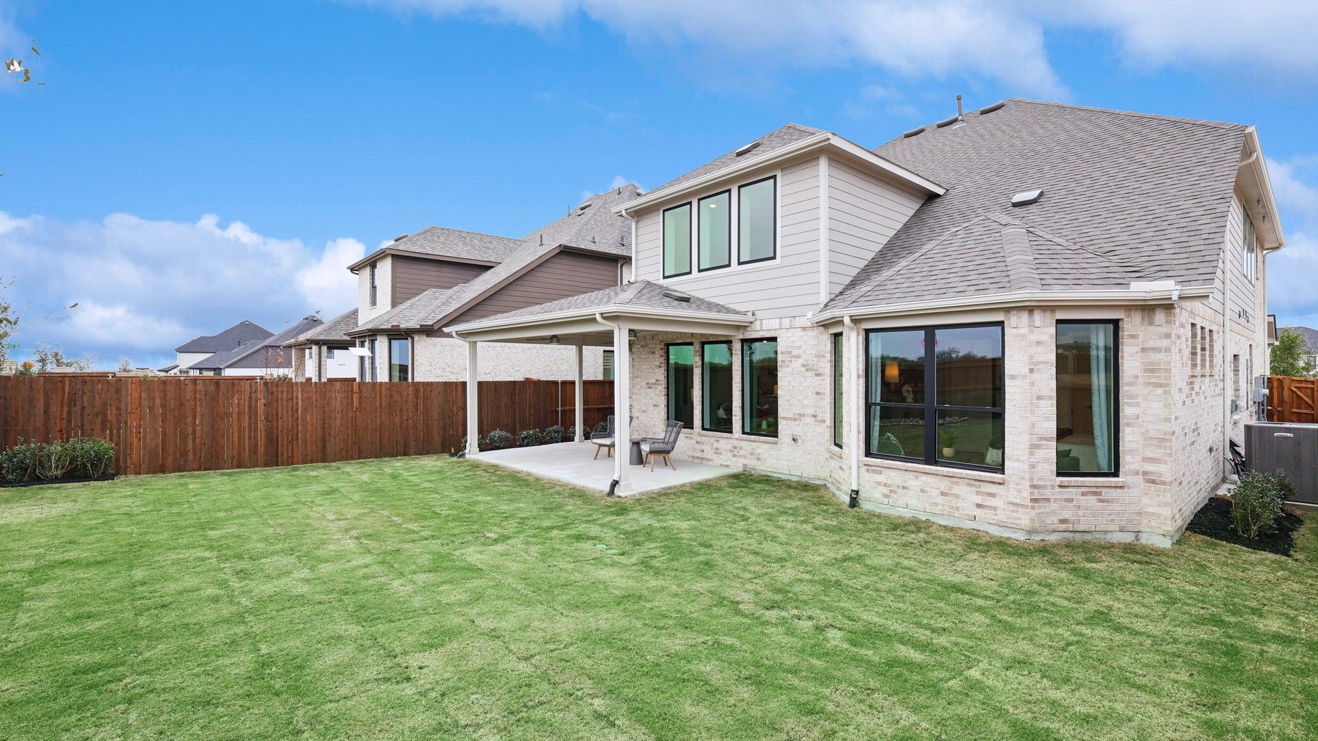 Elegant brickwork and a serene covered patio grace this Wildflower Ranch estate, offering a lush green lawn.