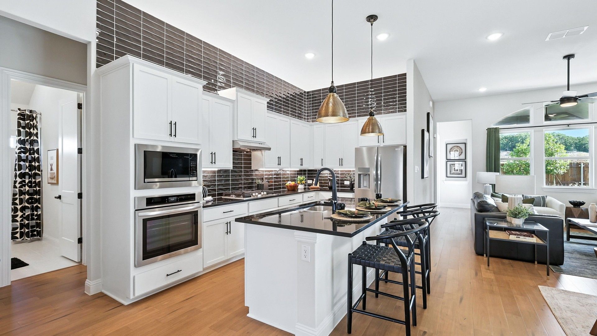 Elegant kitchen features chic black countertops, pendant lighting, and exquisite wood flooring in Green Oaks Preserve.