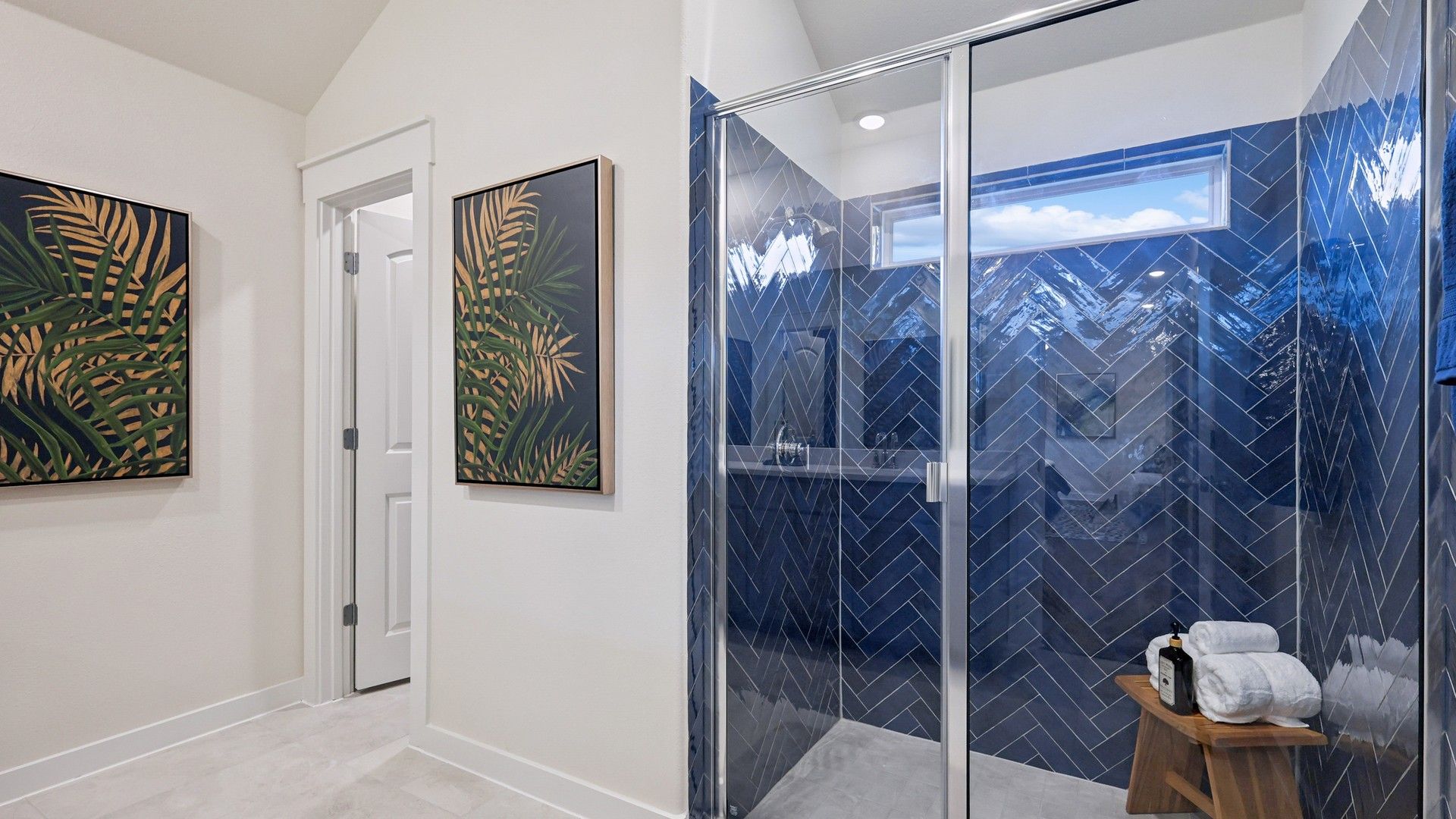 Indulge in this luxurious Churchill bathroom featuring bespoke blue herringbone tiles and striking tropical wall art.