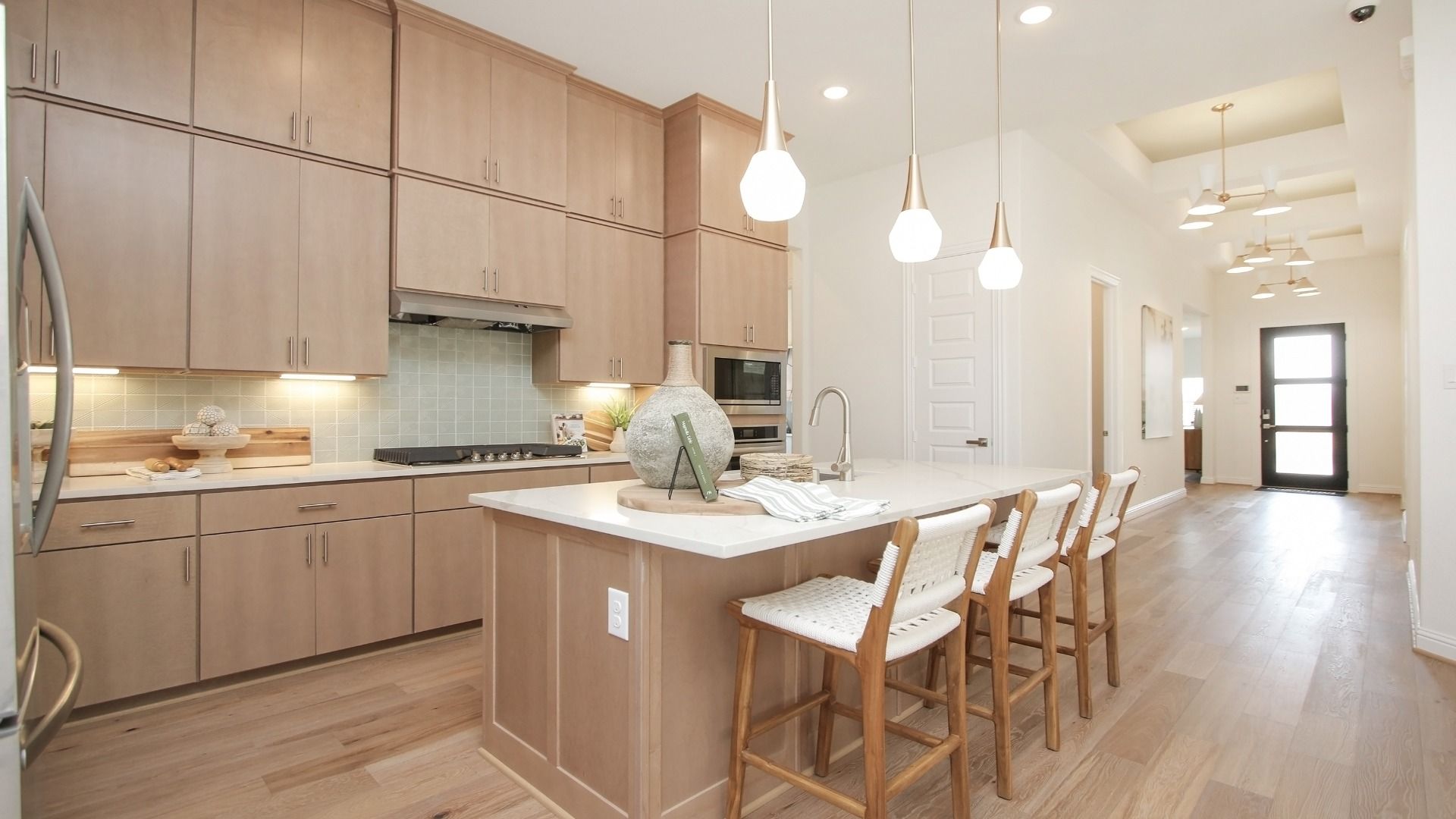Experience luxury in Sunterra's kitchen featuring light wood cabinetry, sleek pendant lighting, and spacious island.