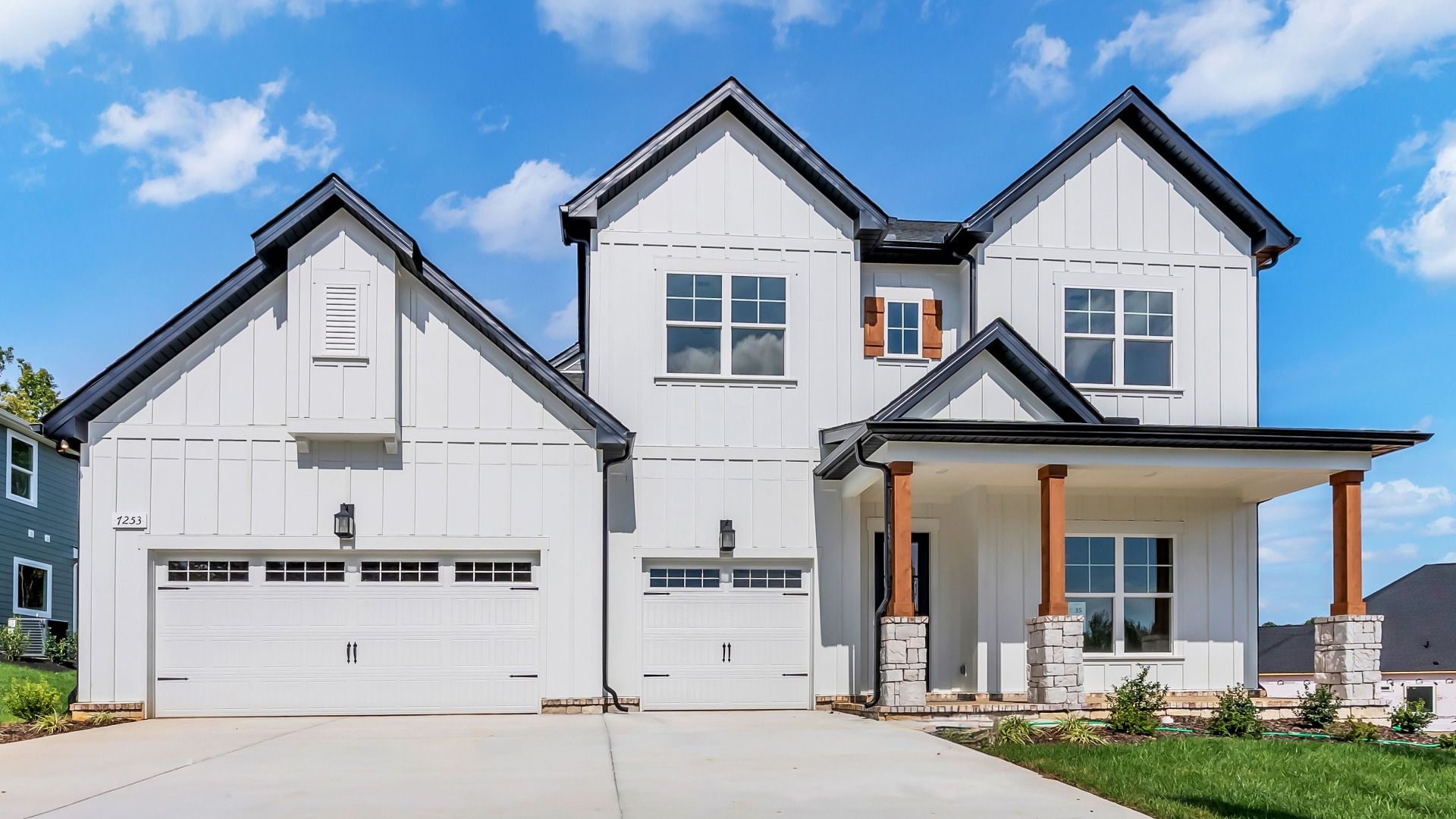Experience elegant design with white vertical siding, wooden shutters and stone pillars in Brush Creek.