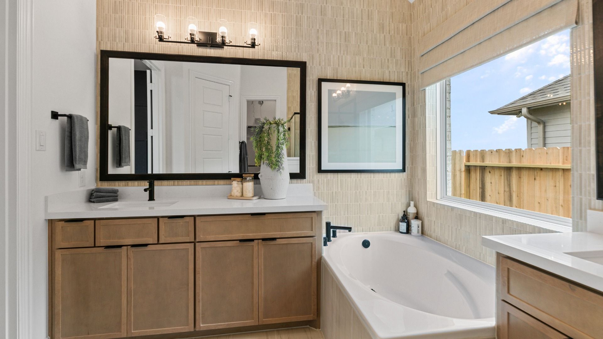 This bathroom in Aldeana features dual sinks and a stylish tiled accent wall.