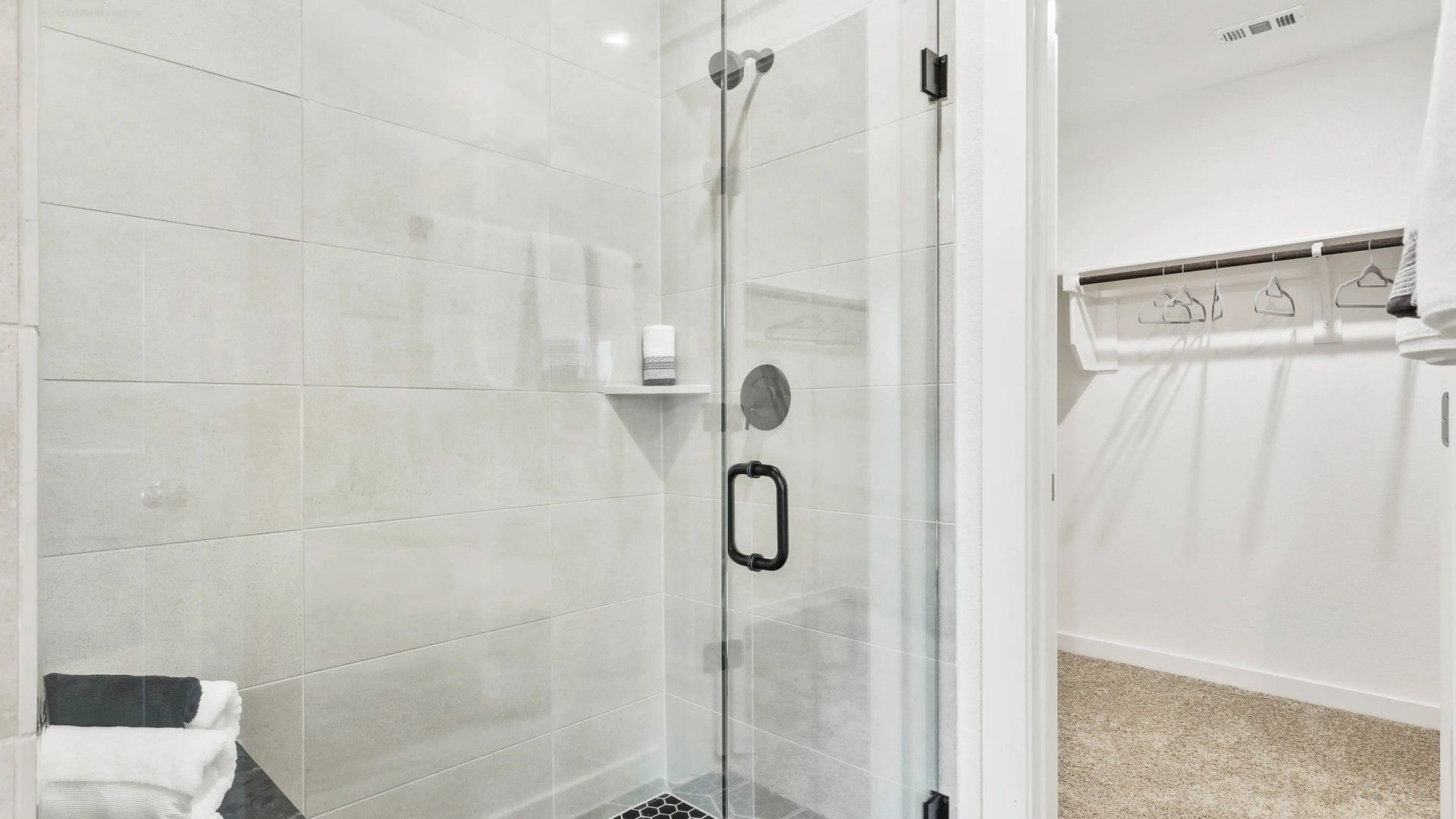 Elegant glass shower with sleek black fixtures and hexagon tile floor, adjacent to walk-in closet, Simpson Crossing.