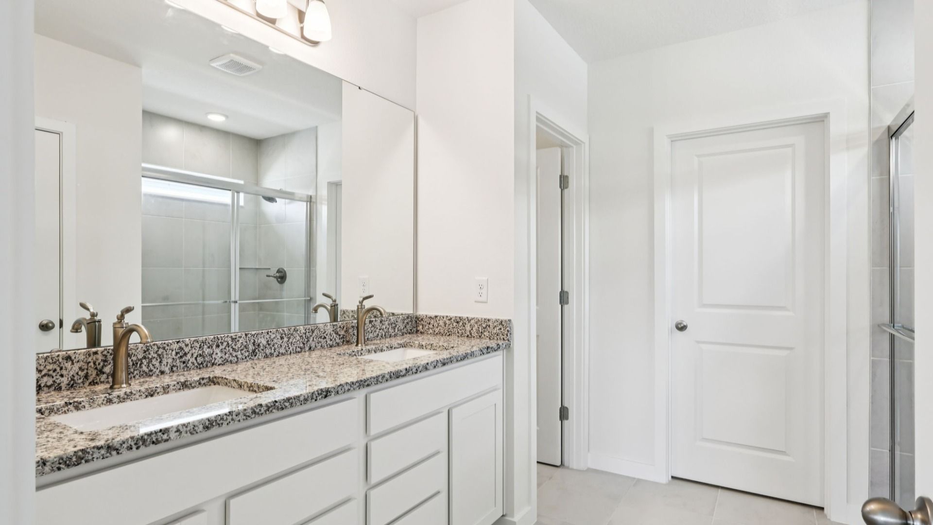 Primary Suite Bathroom with Granite Countertops, Dual Sinks, and White Cabinets in the Baker by DRB Homes Willowbrook North