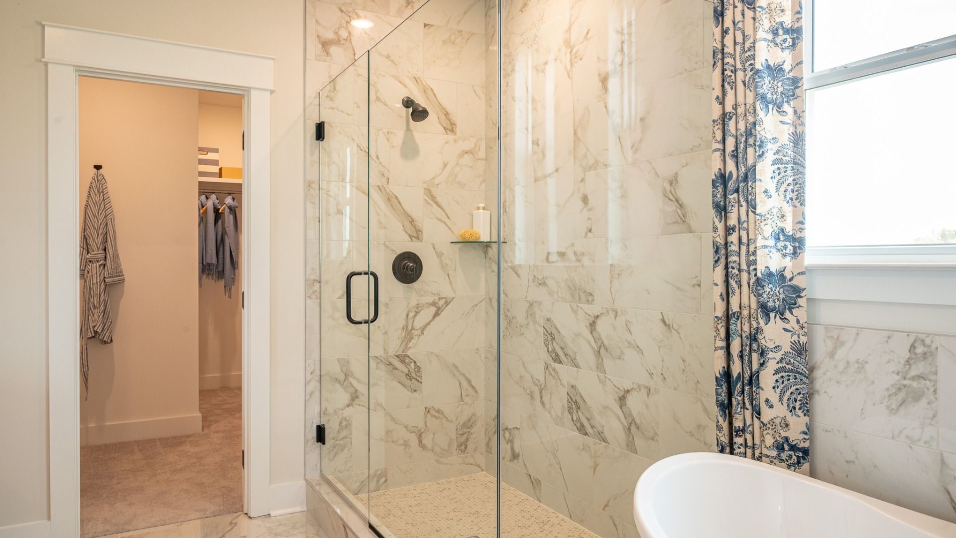 Bright bathroom with frameless glass shower and full tile, separate freestanding tub, and large closet