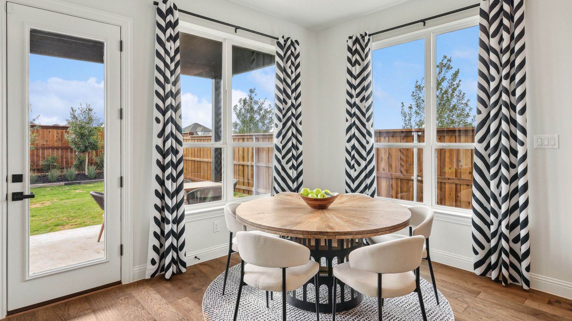 Revel in a chic dining area featuring a round wood table, striking curtains, and expansive windows in Green Meadows.