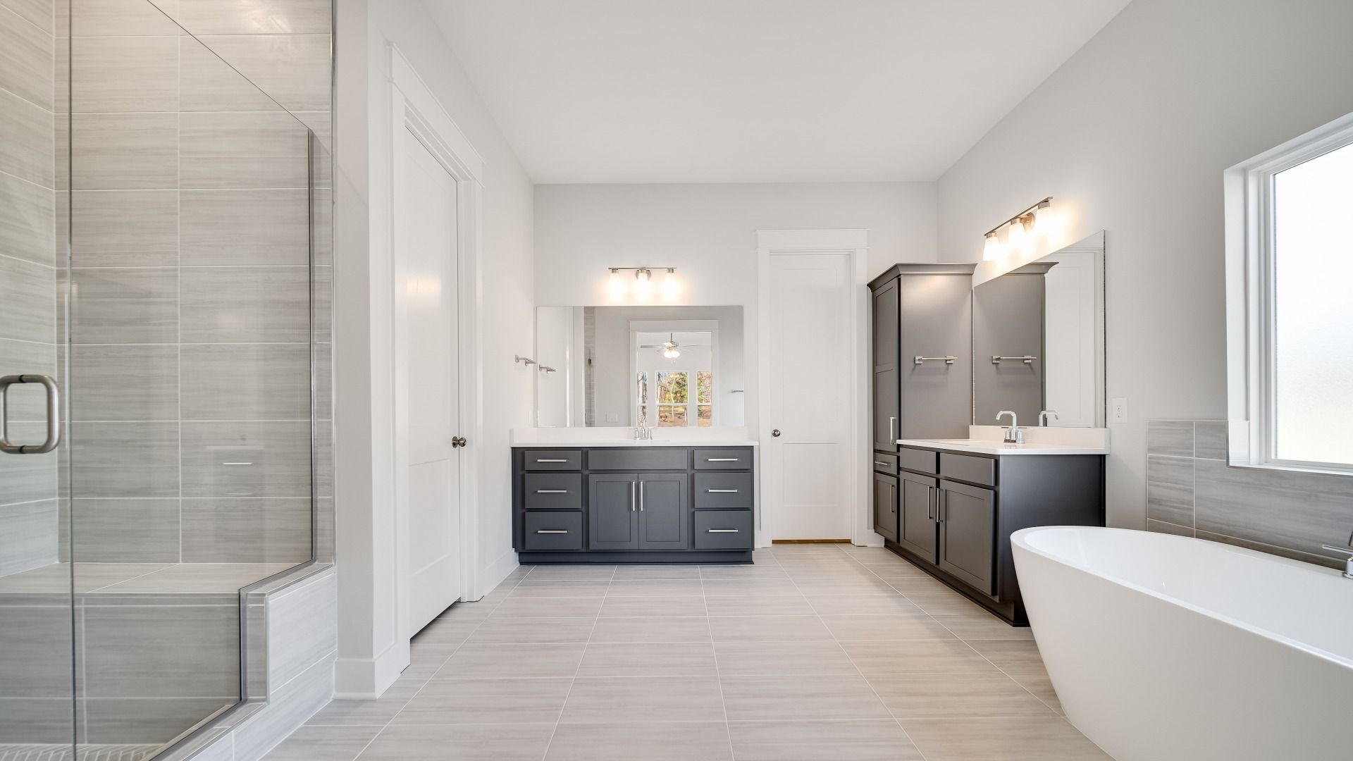 Large bathroom with tiled and glass shower, freestanding tub and modern gray cabinetry and vanity