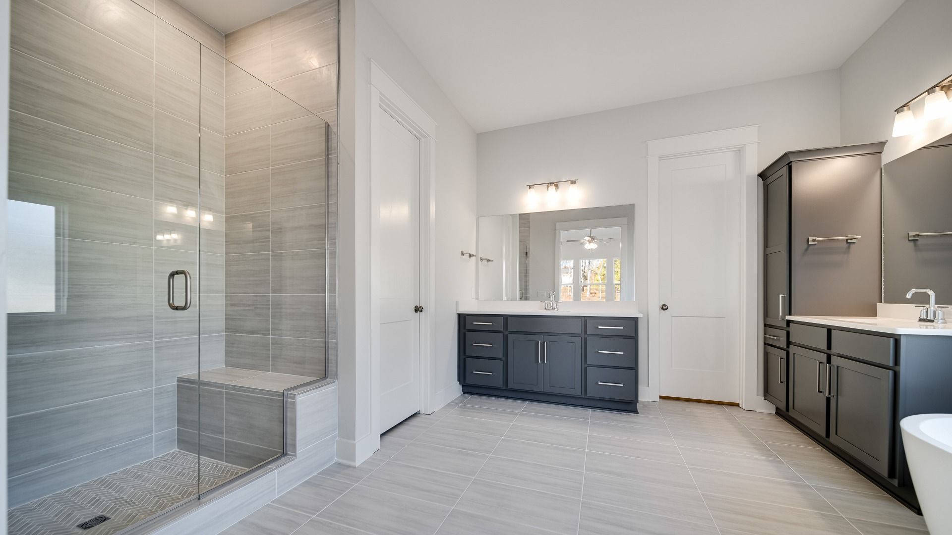 Large bathroom with tiled and glass shower, freestanding tub and modern gray cabinetry and vanity