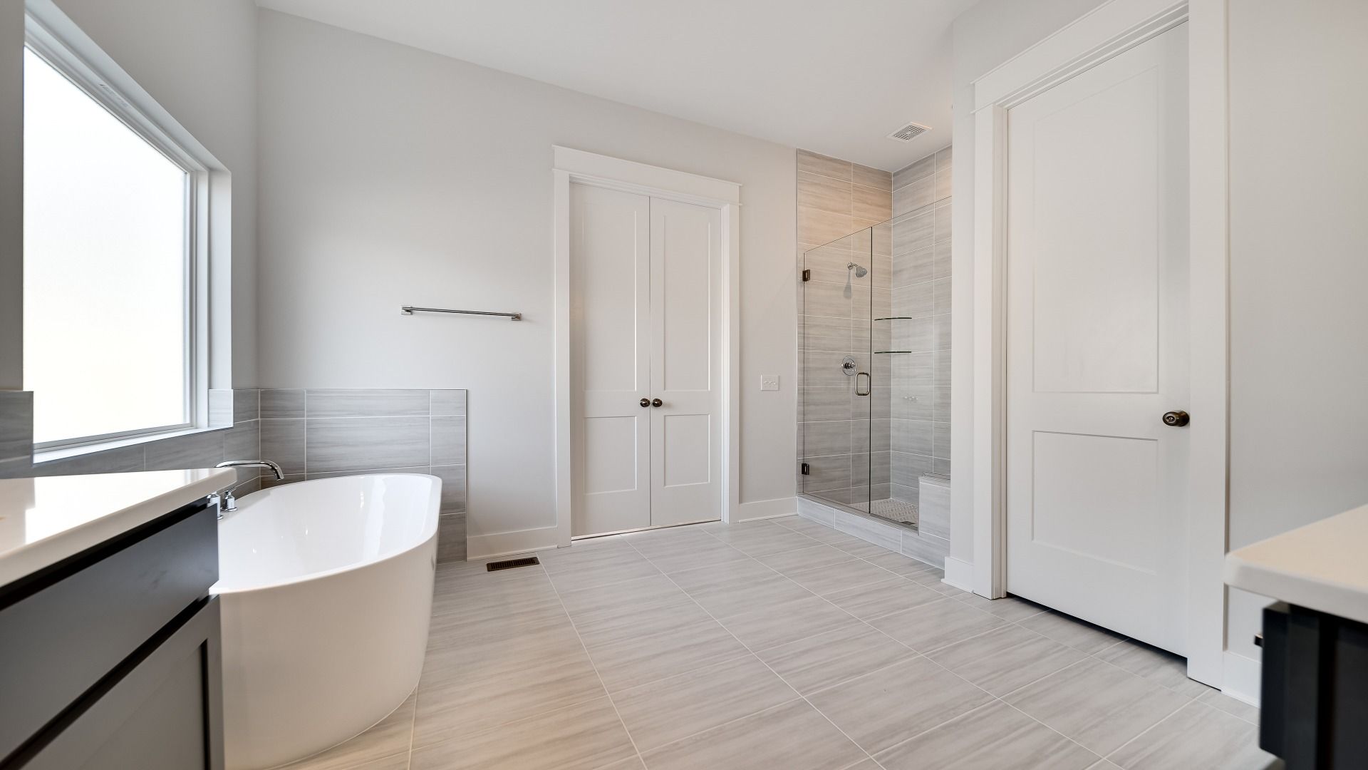Large bathroom with tiled and glass shower, freestanding tub and modern gray cabinetry and vanity