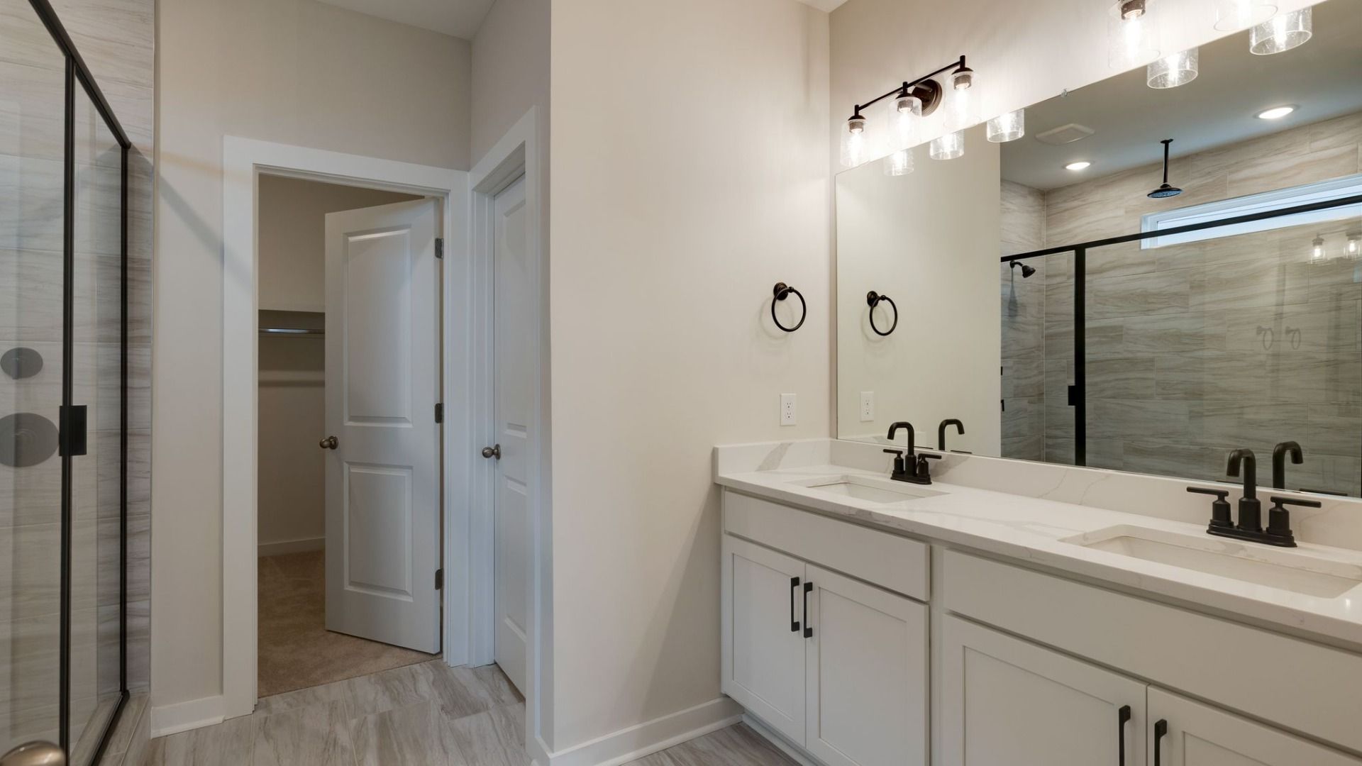 Bathroom with tile floor, walk-in closet, double vanity, and glass and tile shower