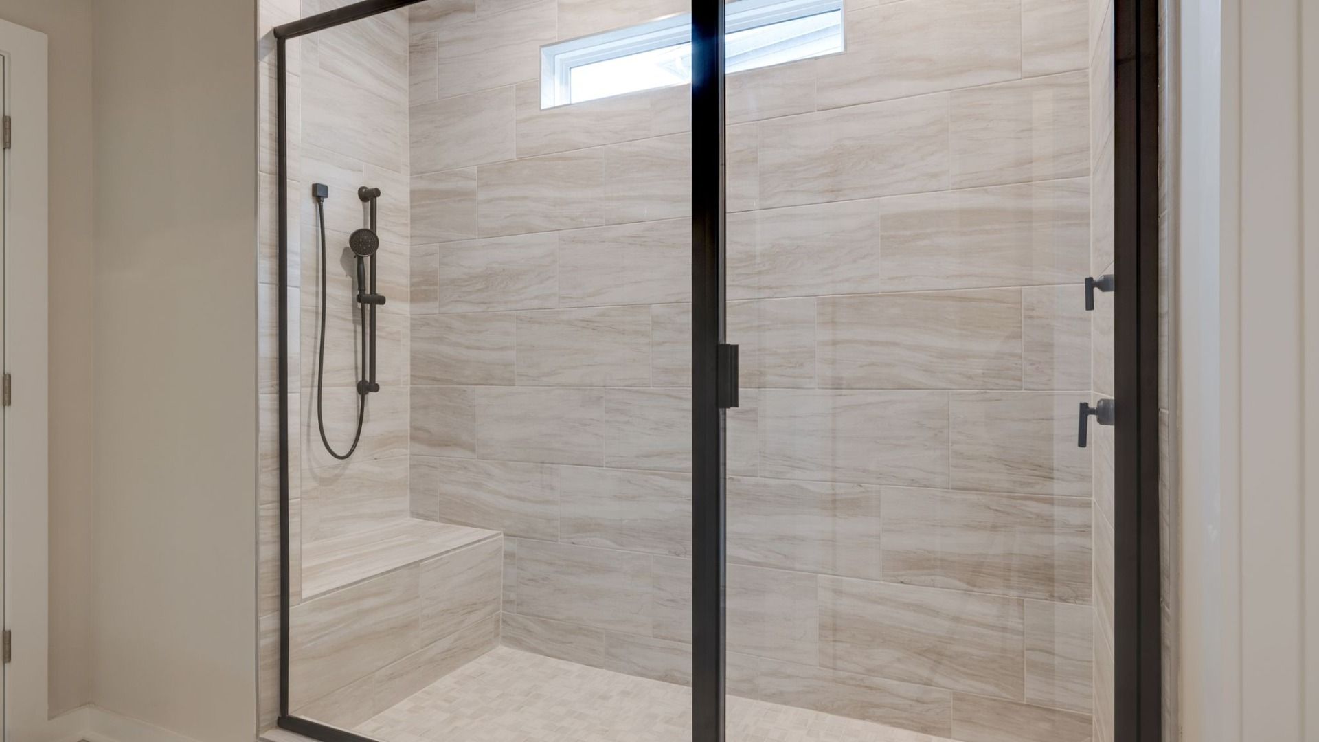 Shower with sleek glass enclosure and tiled walls, floor, and bench