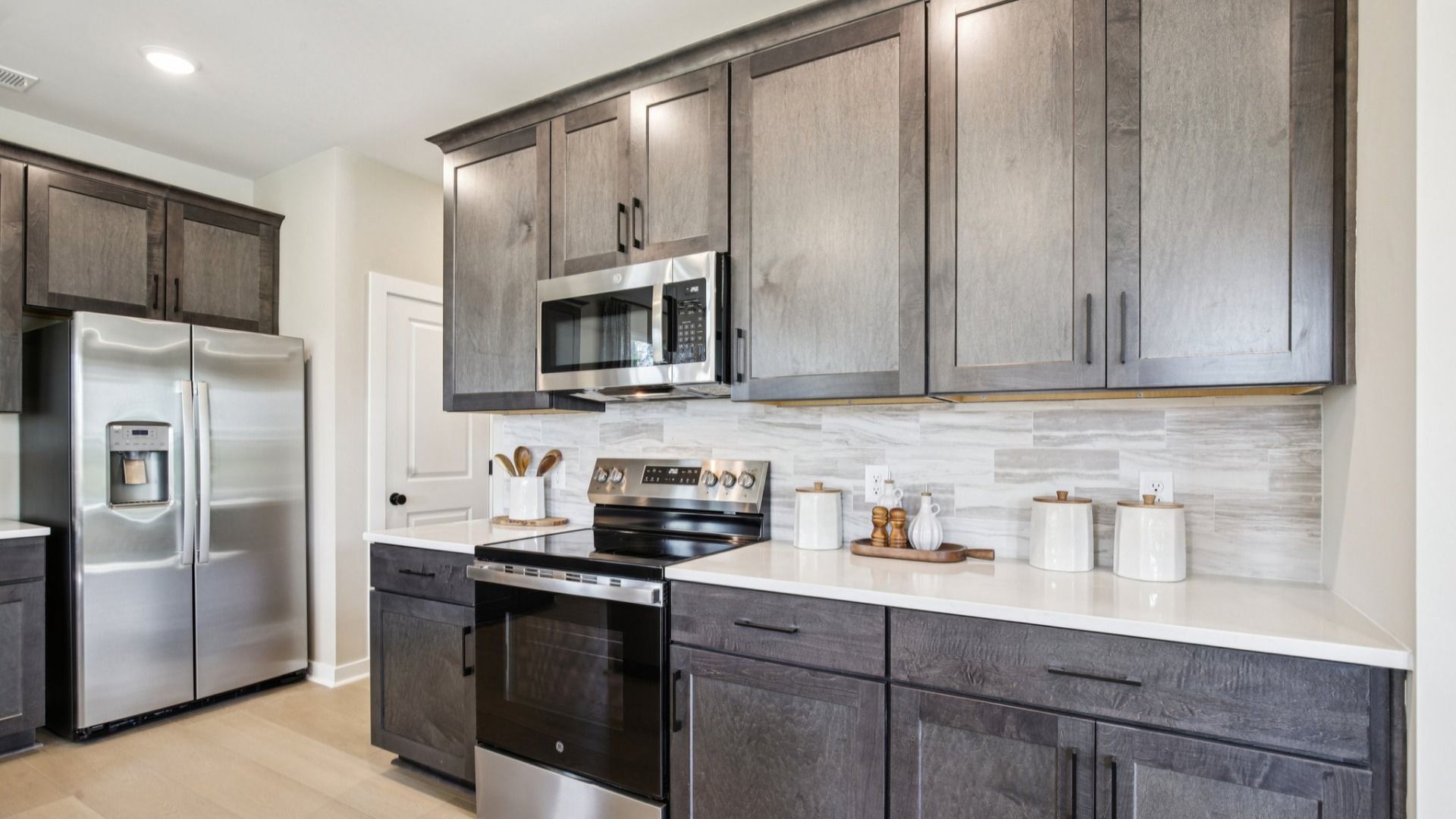 Kitchen with stained gray cabinetry, white quartz countertop, and light tile backsplash