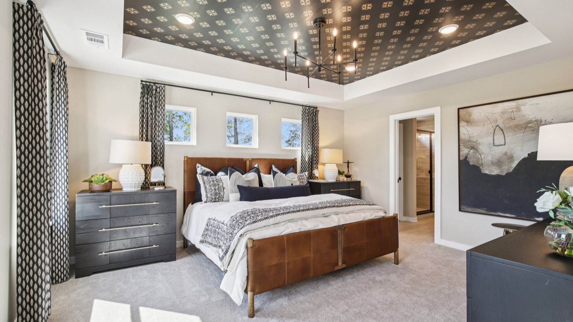 Large primary bedroom with accent tray ceiling and multiple windows for natural light