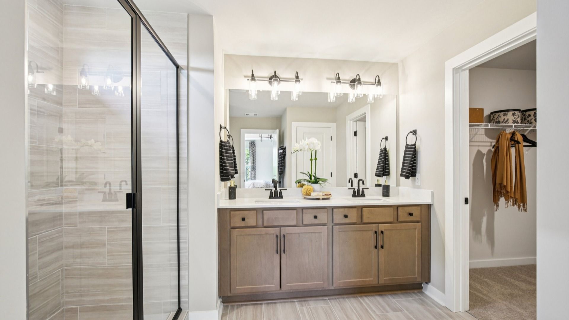 Bathroom with dual-vanity quartz countertop, glass shower enclosure, and primary closet