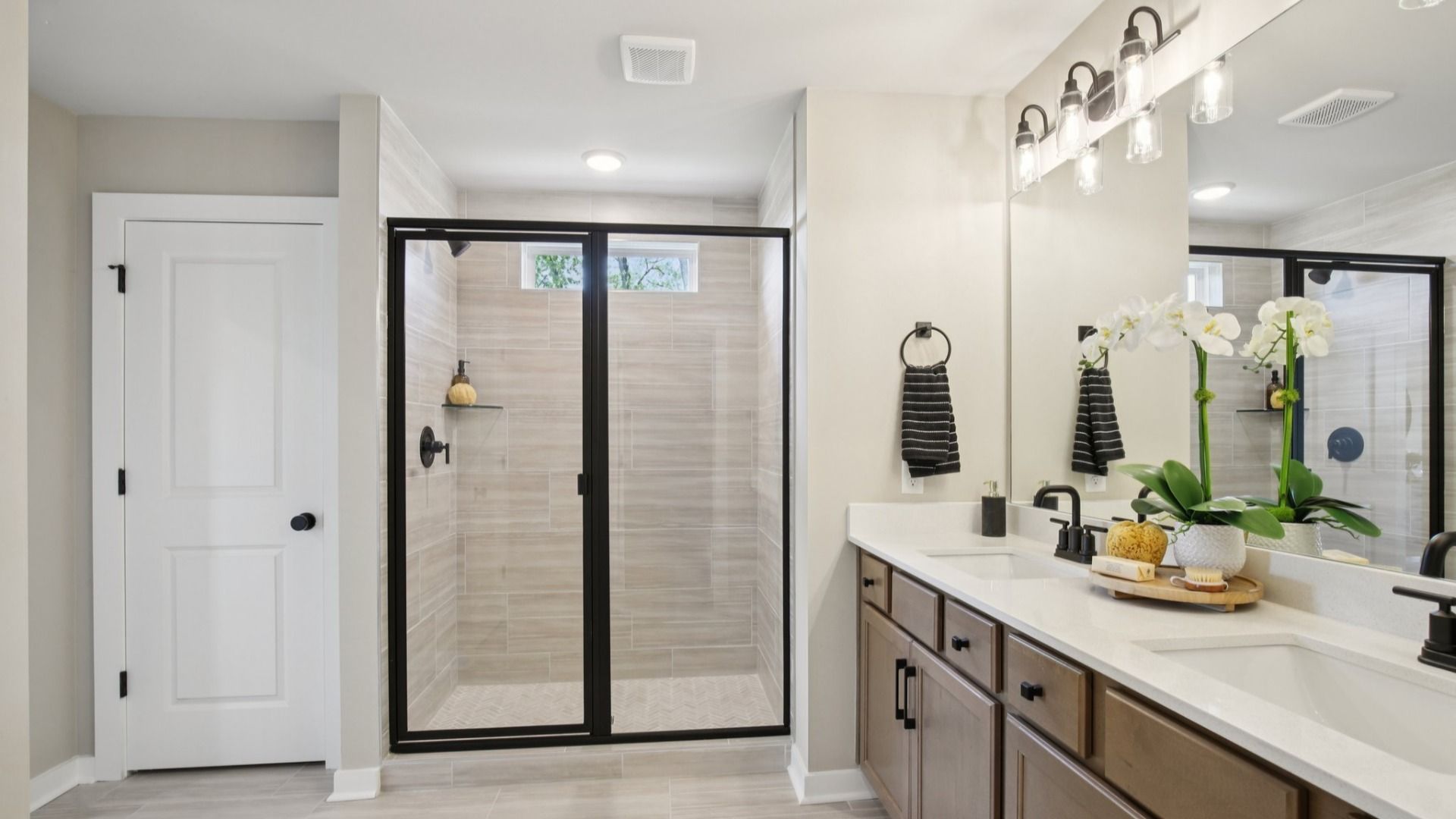 Bathroom with dual-vanity quartz countertop, glass shower enclosure, and linen closet
