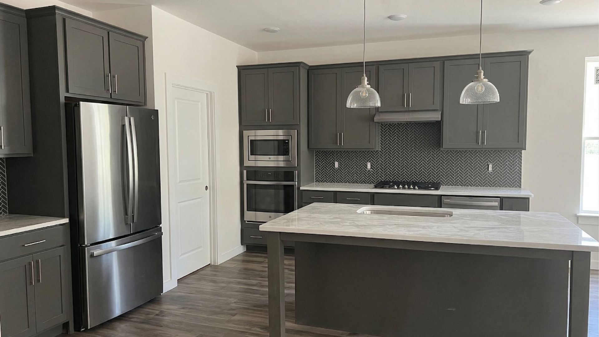 Kitchen with quartz countertops, island, pantry, appliances, and tile backsplash